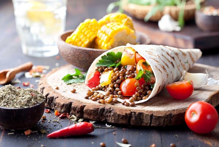 Vegan tortilla wrap, roll with grilled vegetabes and lentil and boiled corn cob on a wooden background