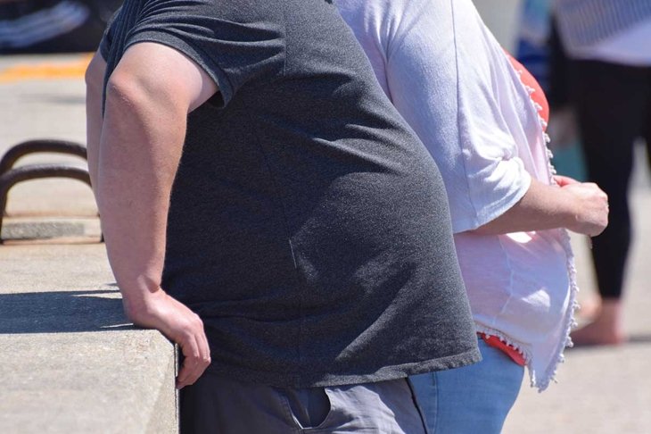 Dorset, UK. May 25 2020. An obese couple standing against a wall in the street. Research shows evidence that obesity and obesity-related conditions seem to worsen the effect of Coronavirus COVID-19.