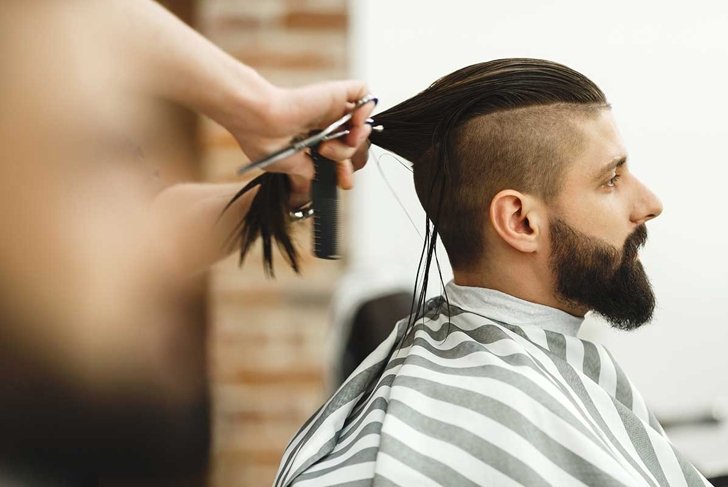 Man\'s hands doing a haircut for man with dark long hair and beard at barber shop, close up portrait, copy space.